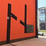 Rote gestrichene Hauswand in den Kölner Rheinhöfen mit Logo und Wegeleitsystem-Tafel